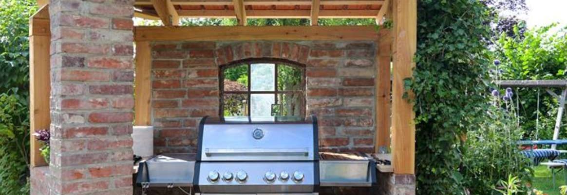 Moderner Stahlgasgrill in einem Unterstand aus alten Ziegeln und Holzkonzept-